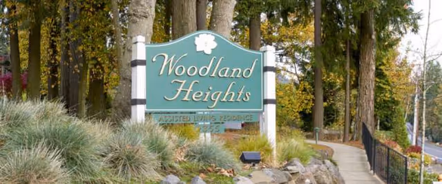 Exterior view of Woodland Heights Assisted Living sign among trees and shrubs.