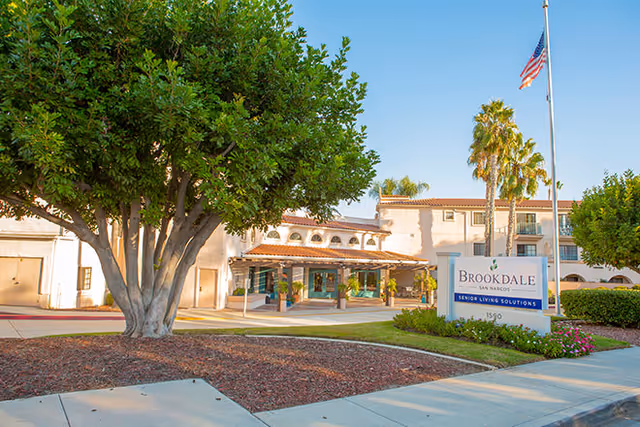 Entrance and sign for Brookdale San Marcos senior living facility with landscaping and an American flag.