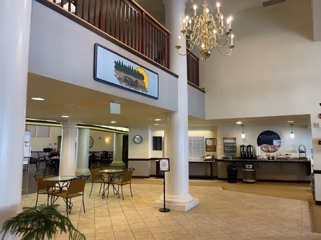 Spacious two-story common area with a chandelier, columns, several small dining tables, and a coffee/buffet counter.