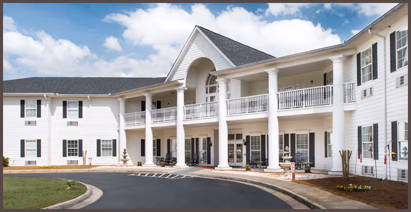 The exterior entrance of Antebellum Grove Senior Living showcasing a white building with columns and a landscaped front.