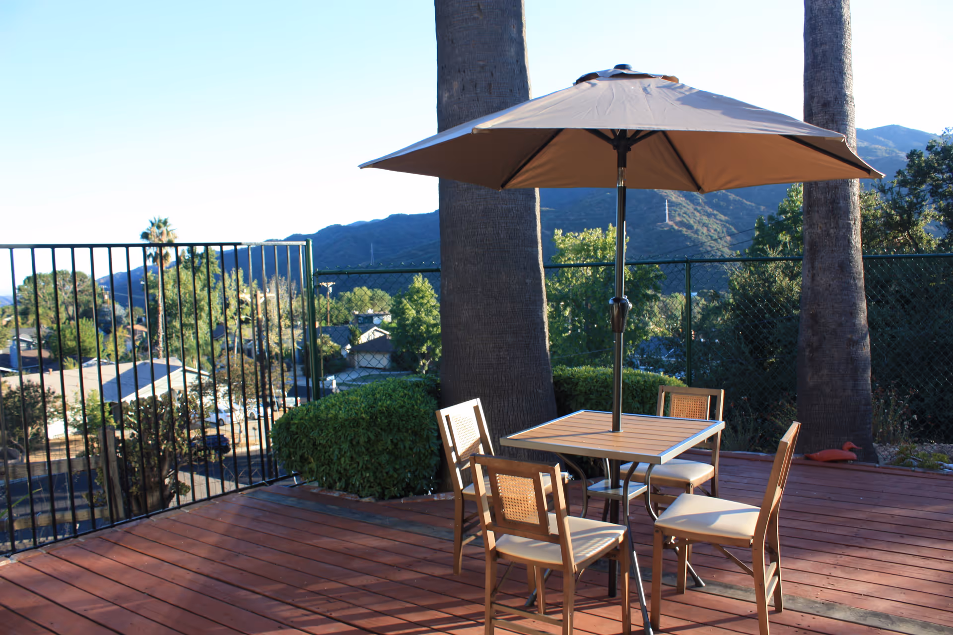 Outdoor terrace with a table, four chairs, umbrella, and mountain view.