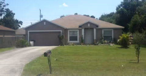 Single-story house with a two-car garage, a driveway, and a well-maintained front lawn with a mailbox and small trees under a clear sky.