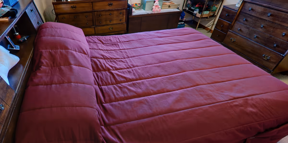 A bedroom with a large bed covered in a red comforter surrounded by wooden dressers and shelving.
