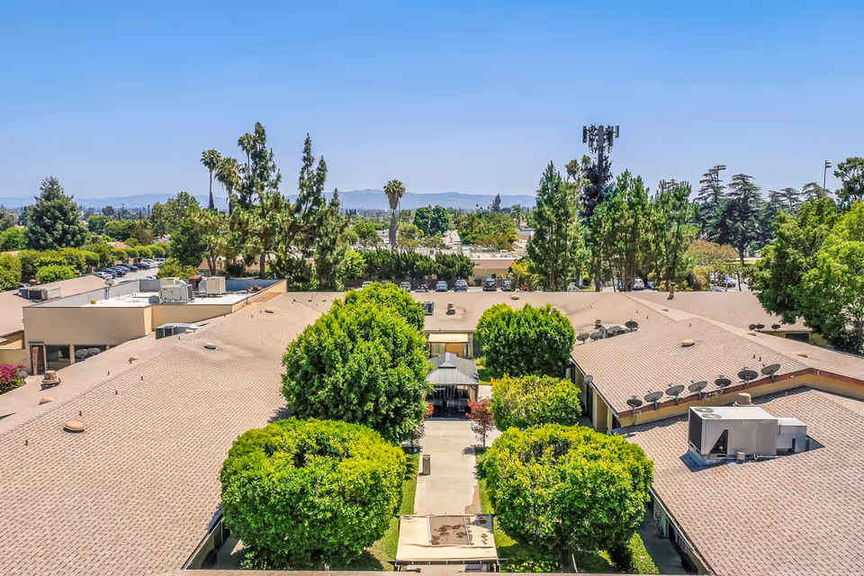 Aerial view of Santa Anita Assisted Living facility showing the rooftops of single-story buildings surrounded by green trees and shrubs under a clear blue sky.