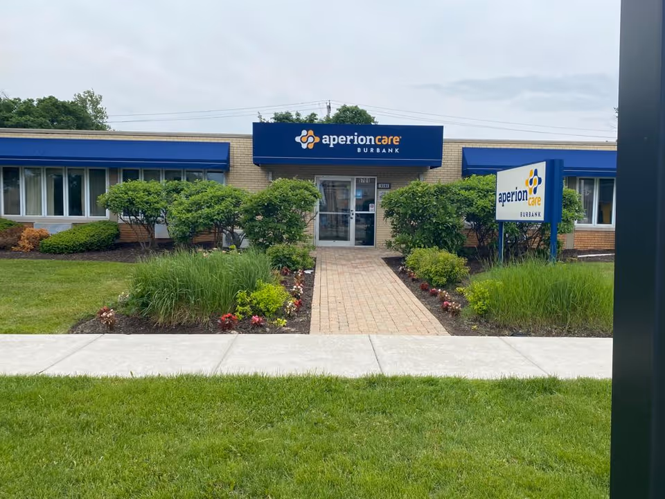 Front entrance of the Aperion Care Burbank building with a brick walkway, landscaping, and signage.
