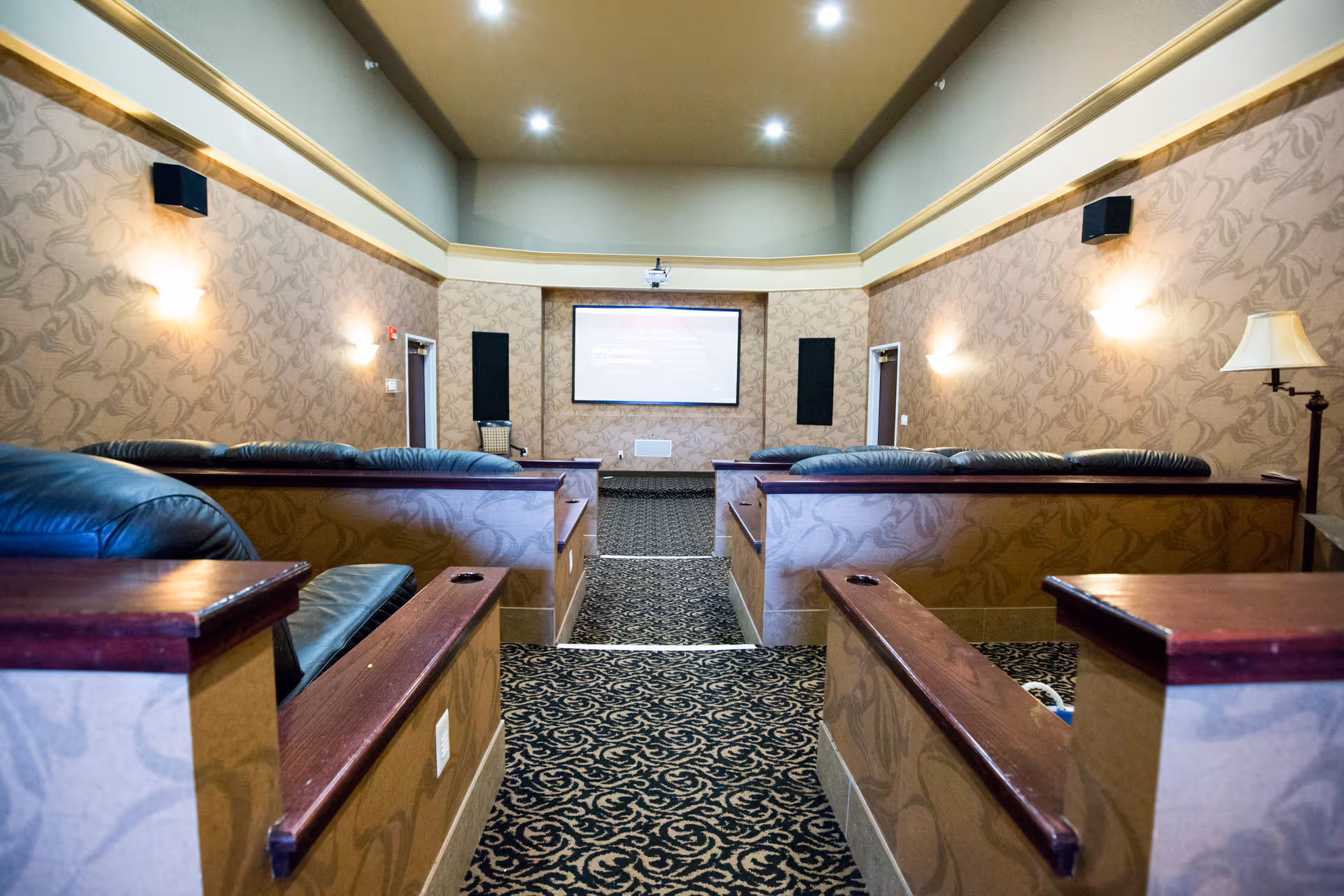 A small community theater/media room with tiered leather seating facing a projector screen.