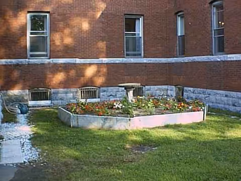 Brick nursing home exterior with a rectangular flower bed and a small central fountain.
