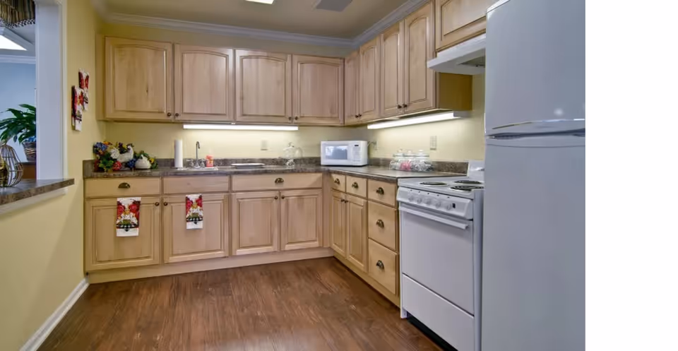 Kitchen with light wood cabinets, granite countertops, a white stove and refrigerator, microwave, and dark wood flooring.
