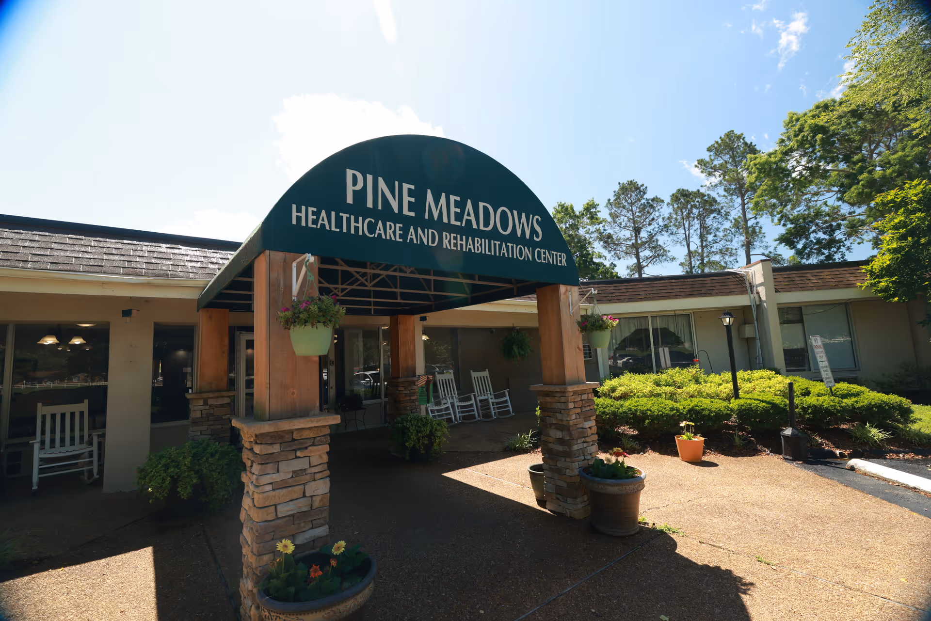 Front entrance of Pine Meadows Healthcare and Rehabilitation Center with a green canopy over the driveway and potted plants.