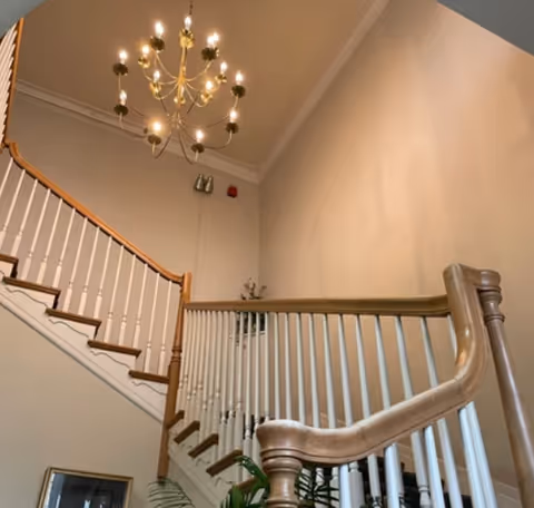 Interior view of a grand staircase with a wooden banister and a multi-arm chandelier over the landing.