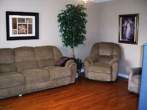 Living room seating area with beige sofa, armchairs, plant, and framed art.