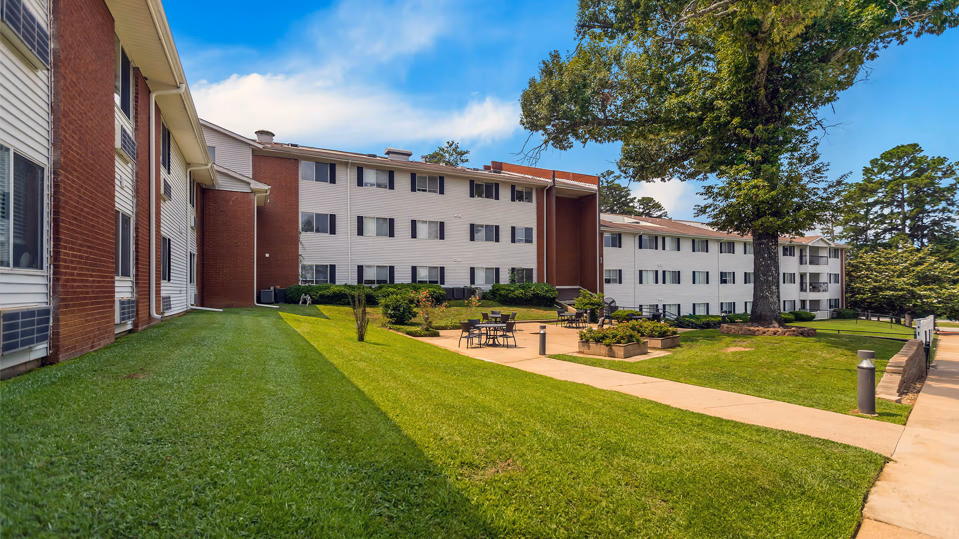 View of the exterior of Colonial Village, showcasing the building's facade, landscaped lawn, and outdoor seating area.