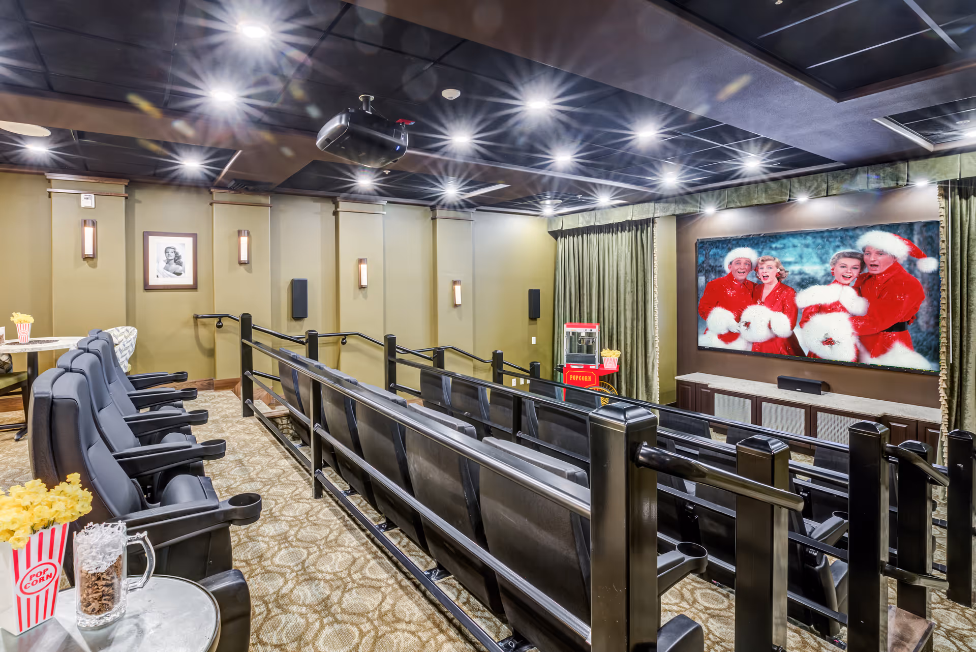 A private screening room with tiered black reclining seats, a large wall-mounted screen showing people in Santa outfits, and popcorn stands.