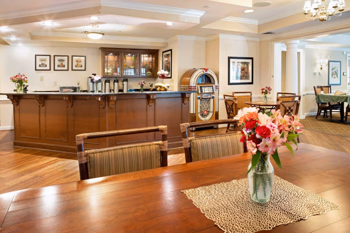 Dining room/common area with wooden tables, a vase of flowers in the foreground, a service counter and a vintage jukebox in the background.