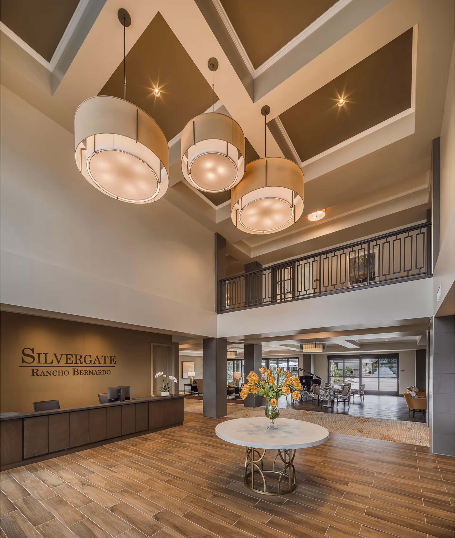 Spacious two-story lobby with a reception desk, round table with flowers, seating area, and large hanging pendant lights.