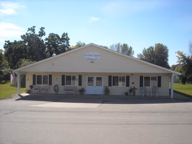 Single-story light-colored building with a covered front porch, central double doors, windows with shutters, and a 'Country Terrace' sign above the entrance.