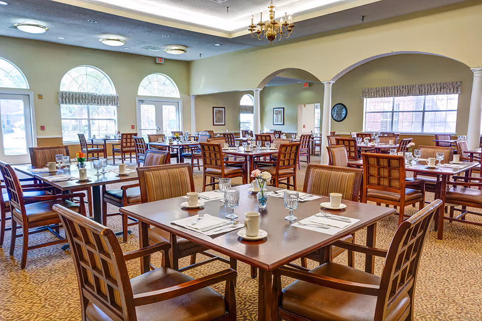 Spacious, well-lit dining room with multiple tables set with cups, glasses, and floral centerpieces.