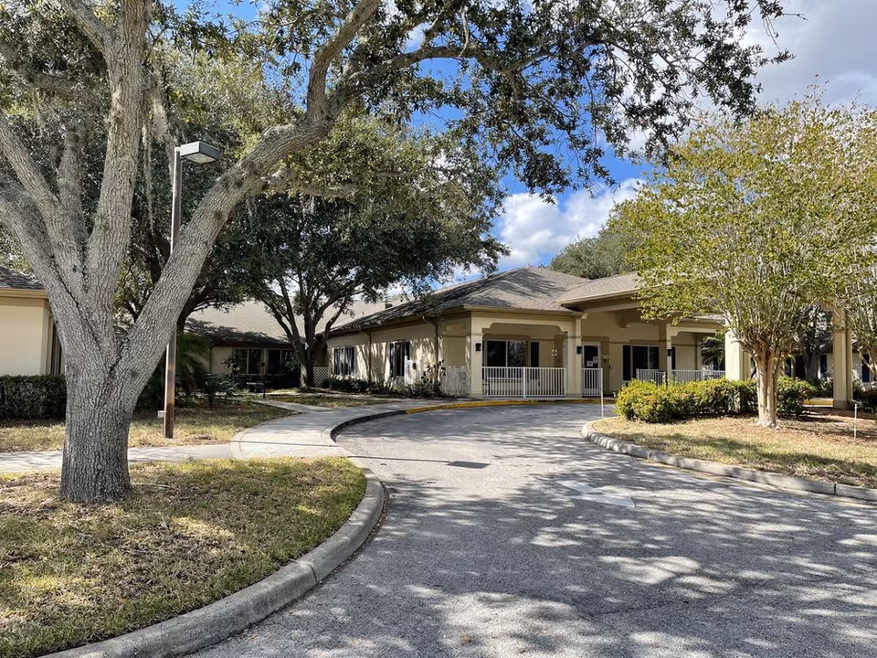 Front entrance of a single-story senior living facility with a circular driveway and trees.