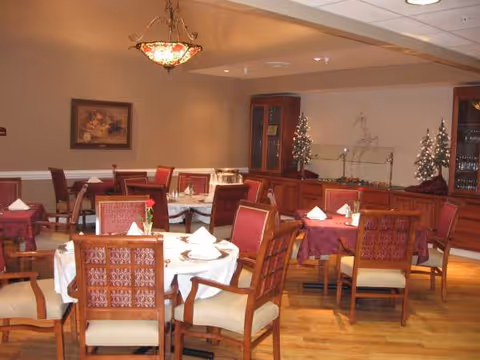 Dining room in a senior living facility with round tables, red chairs, and holiday decor.