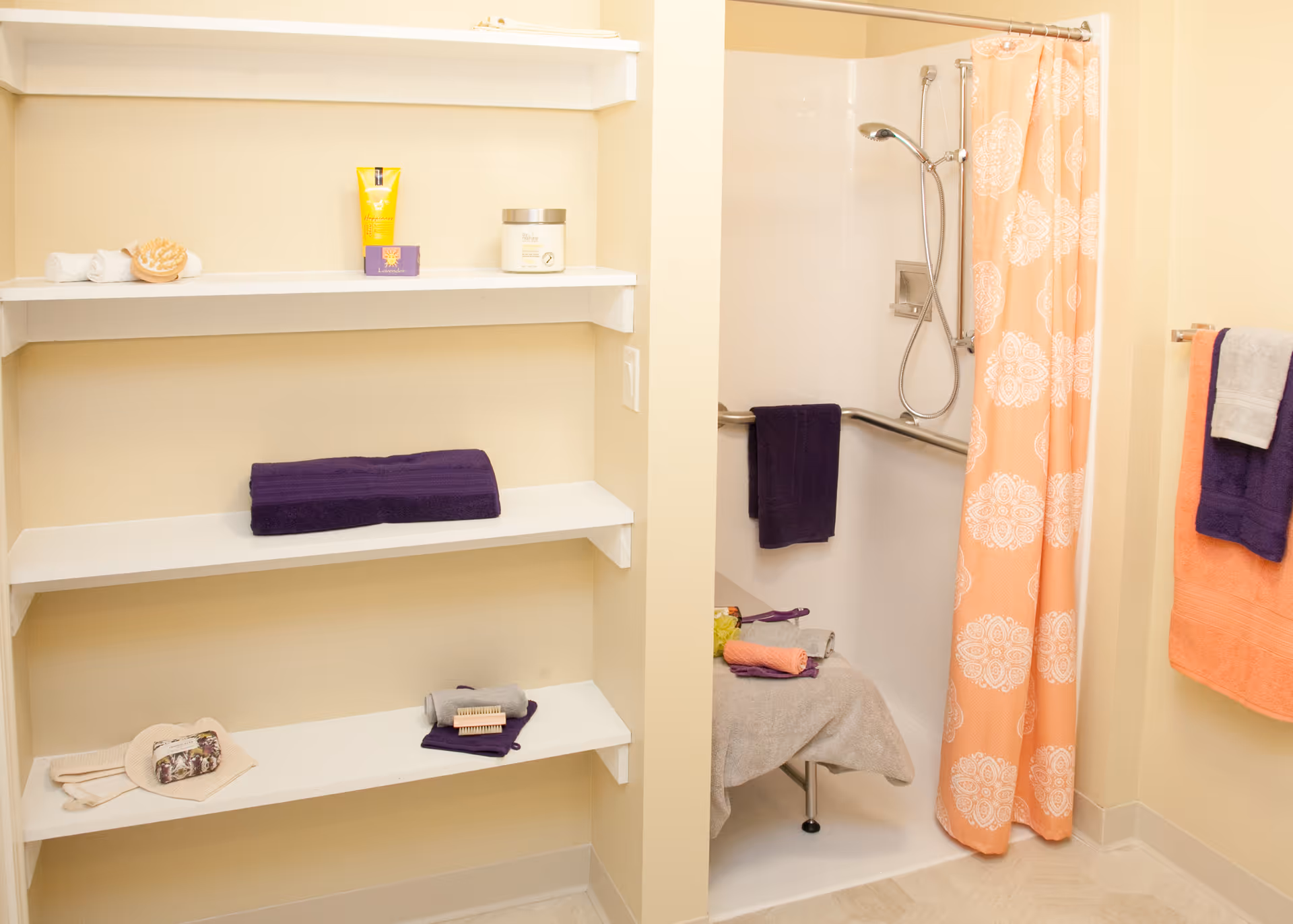 Bathroom with built-in white shelves holding towels and toiletries and an accessible shower with a peach-patterned curtain.