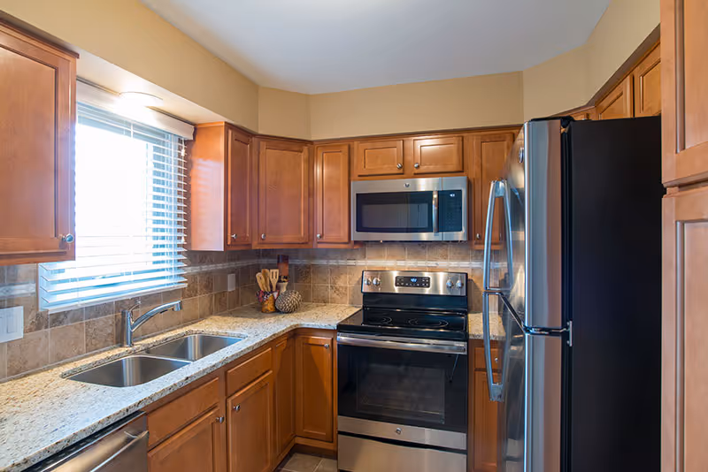 Kitchen with wooden cabinets, granite countertops, stainless steel appliances, and a sink beneath a window.