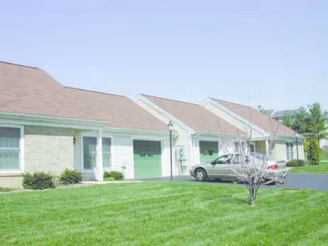 Row of cream-colored senior residences with green garage doors and a manicured lawn.
