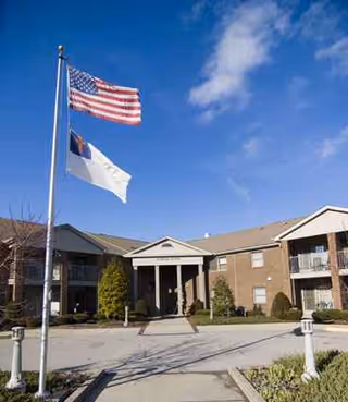 Brick senior living facility exterior with flags, entrance, and manicured landscaping.