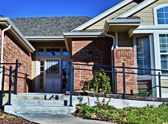 Exterior view of a senior living facility entrance with brick facade, stairs, and railing.