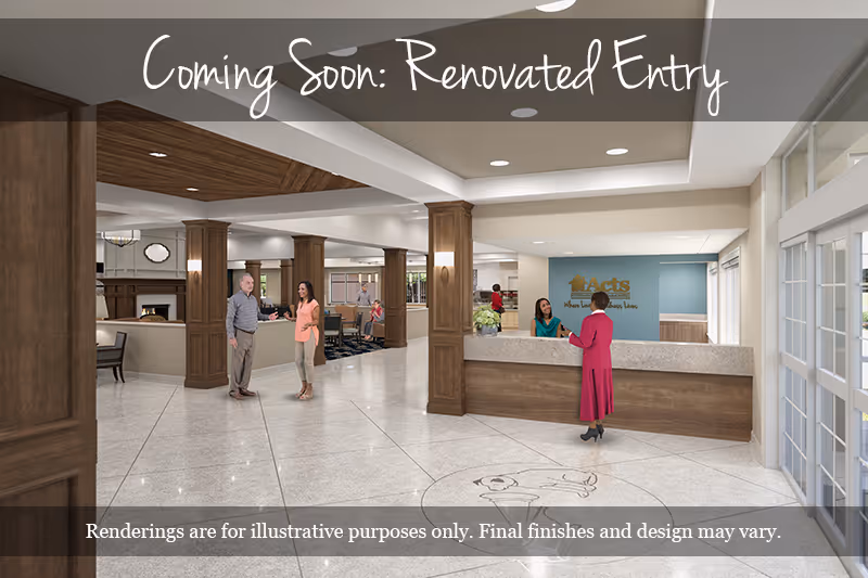 A spacious senior living facility entry area with a reception desk on the right where a woman in a red dress is speaking to a receptionist. Two people are conversing near wooden columns in the middle of the room. The area features polished tile floors, wooden accents, and large windows allowing natural light. A sign behind the reception desk reads 'Acts Where Love and Compassion Live.'