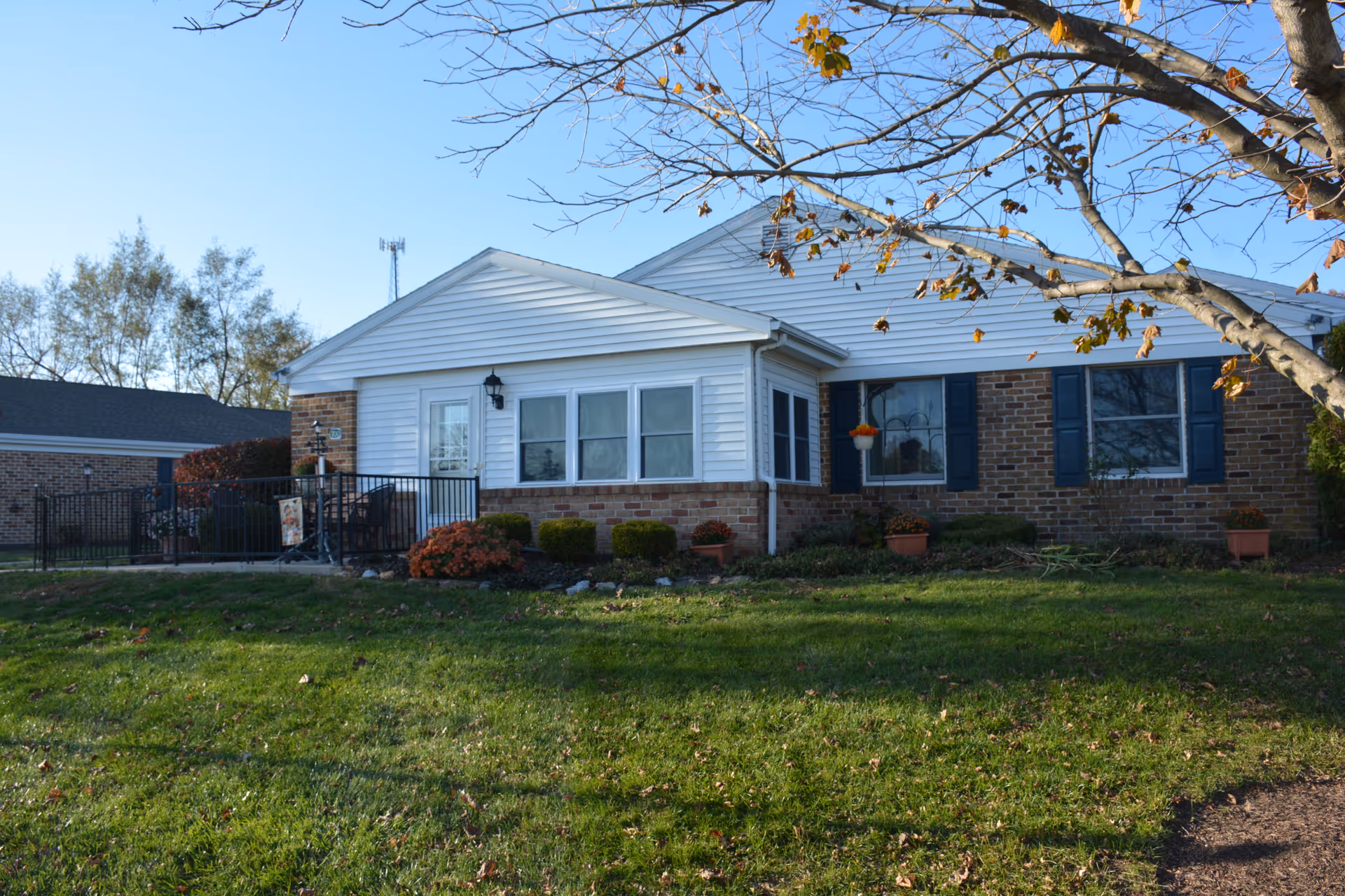 Single-story brick and white-sided building with a small porch, potted plants, and a grassy front lawn under a clear sky.