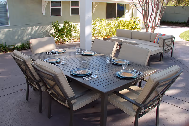 Outdoor patio with a dining table set for six and cushioned lounge seating under a covered pergola.