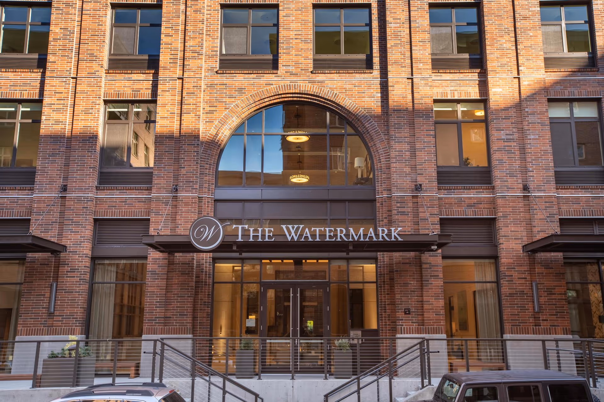 Brick facade and main entrance of The Watermark senior living building featuring a large arched window and canopy sign.