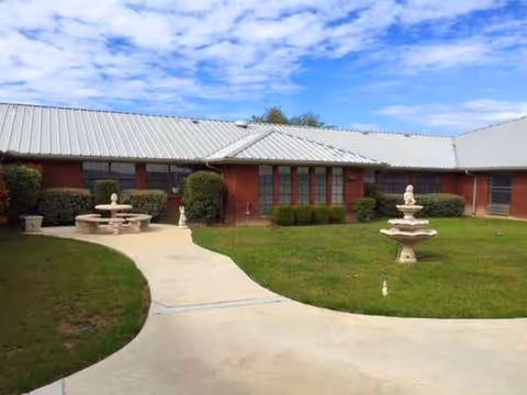 Front exterior of a single-story red-brick senior living facility with a courtyard and fountains.