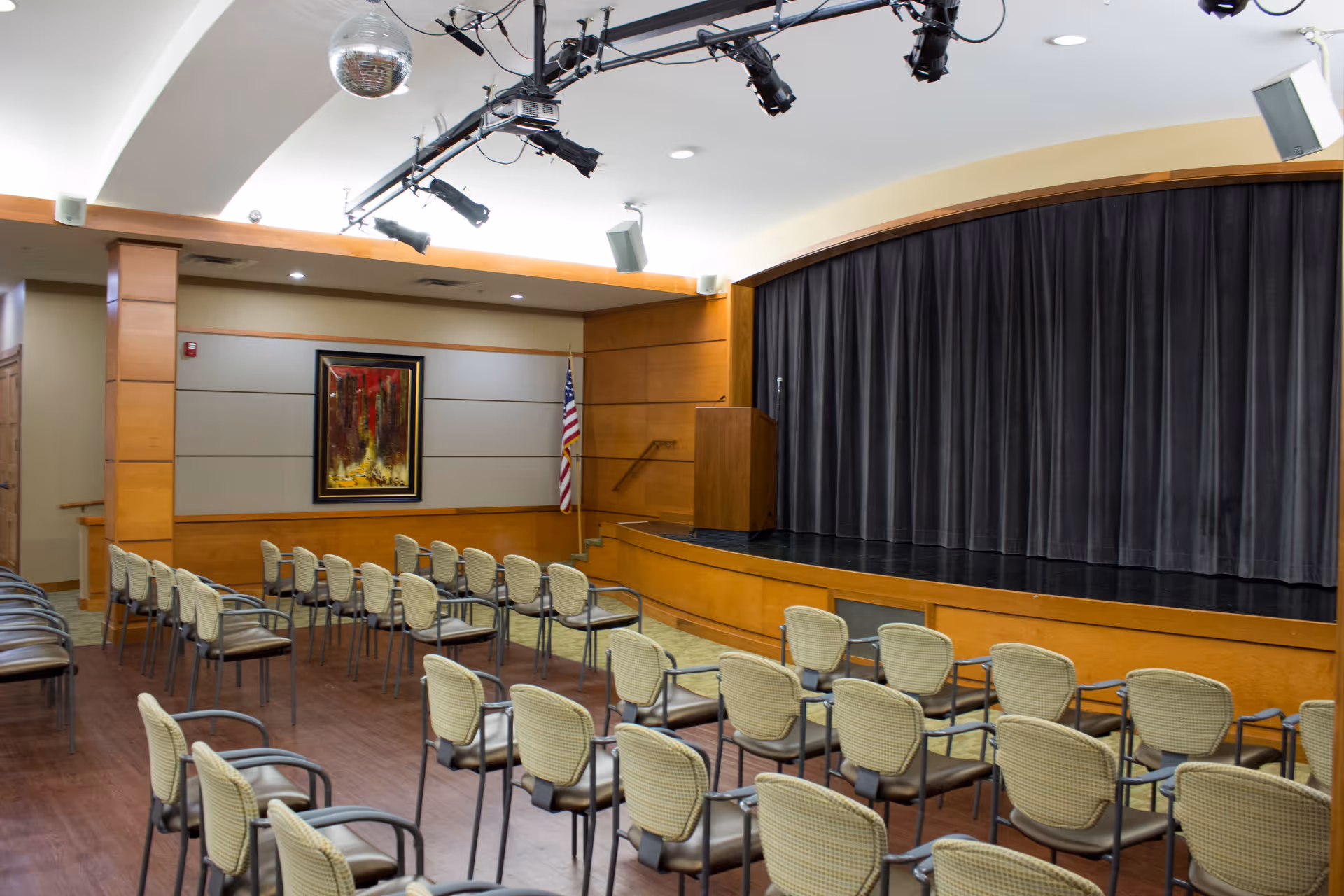 Empty auditorium-style activity room with rows of chairs facing a stage with a closed curtain and podium.