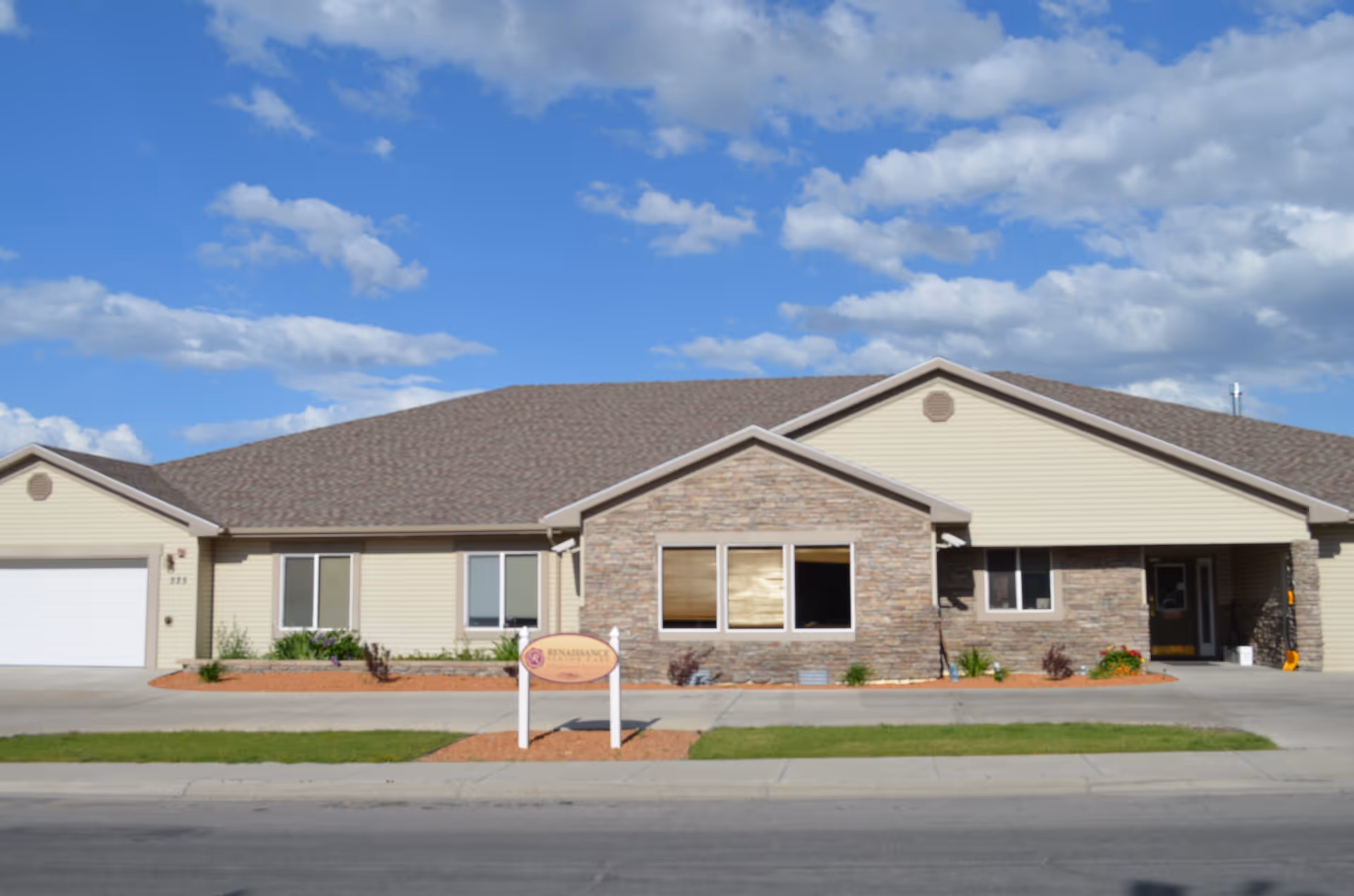 Single-story Renaissance Senior Care building with a stone-and-siding facade, front lawn, and a sign under a blue sky.