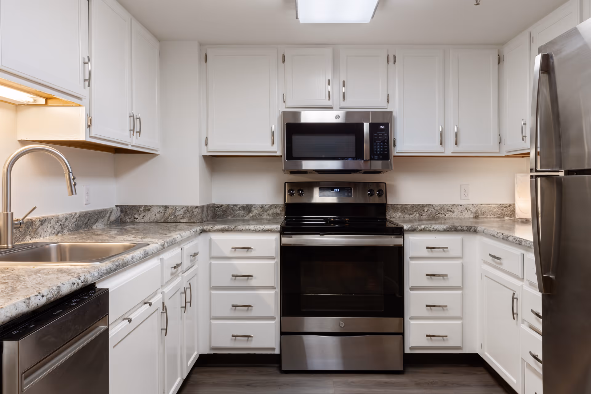 Modern kitchen with white cabinets, granite countertops, stainless steel appliances including a refrigerator, oven, microwave, dishwasher, and a sink with a curved faucet.