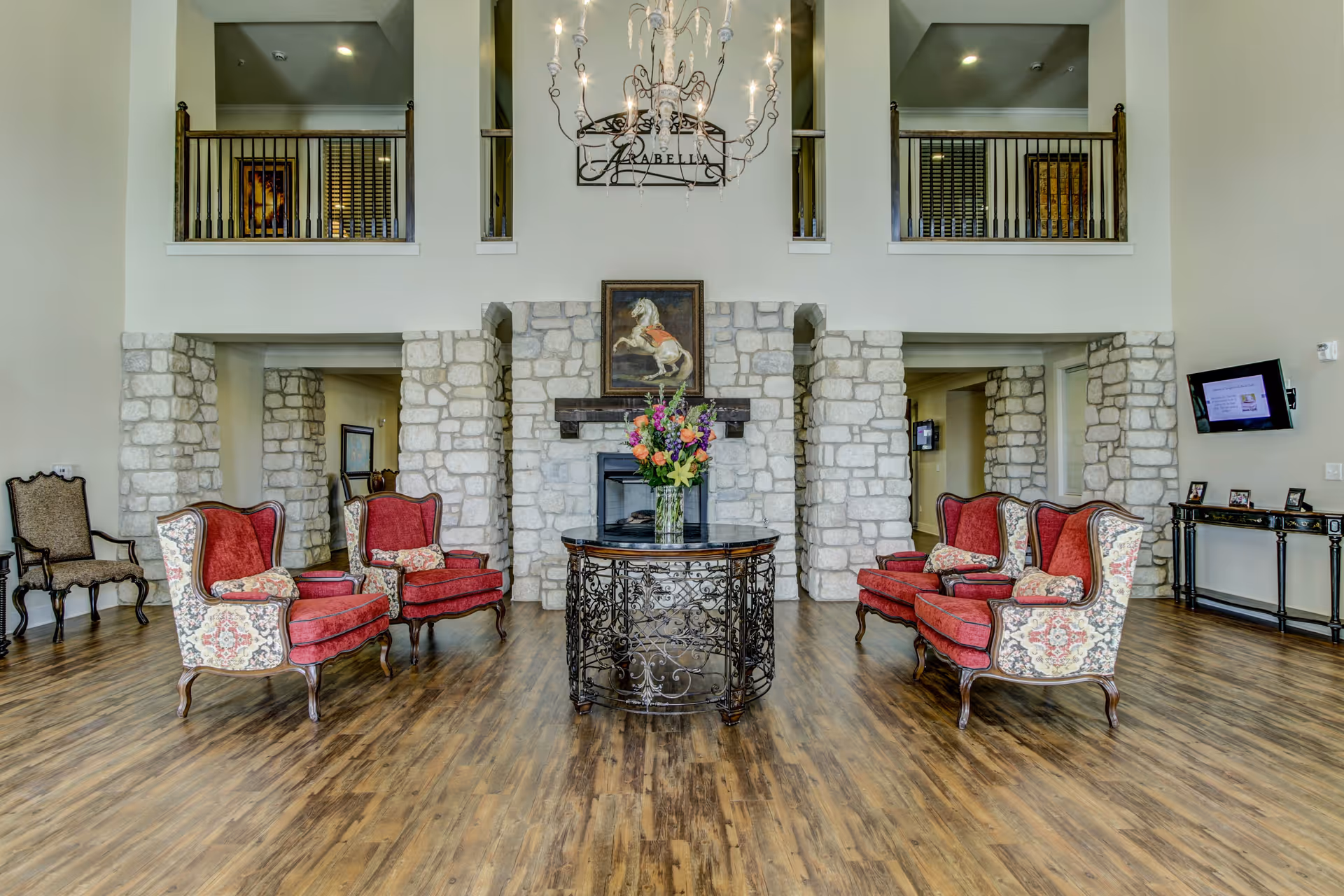 Spacious lobby with a stone fireplace, chandelier, and red upholstered armchairs arranged around a central decorative table.
