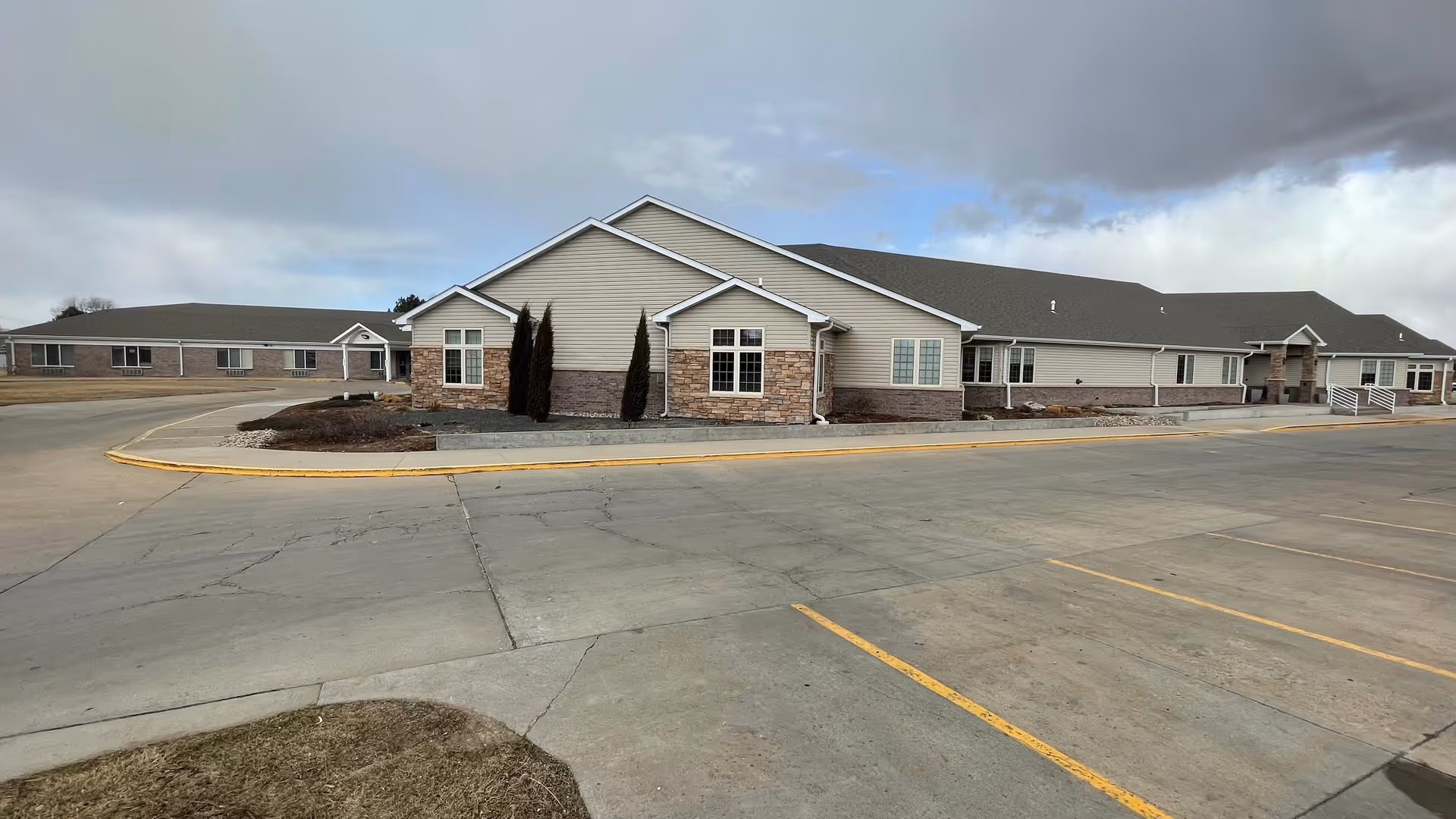 Exterior view of a long, single-story senior living facility with stone accents and a parking lot.