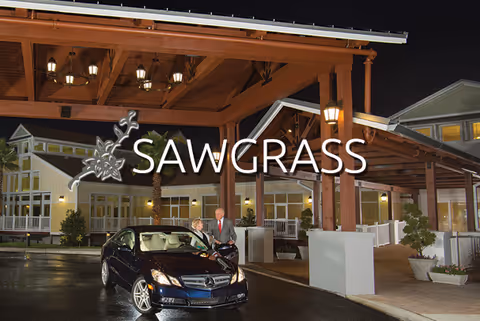 Night view of a facility's covered entrance with a parked car, two people by the vehicle, and 'SAWGRASS' overlaid.