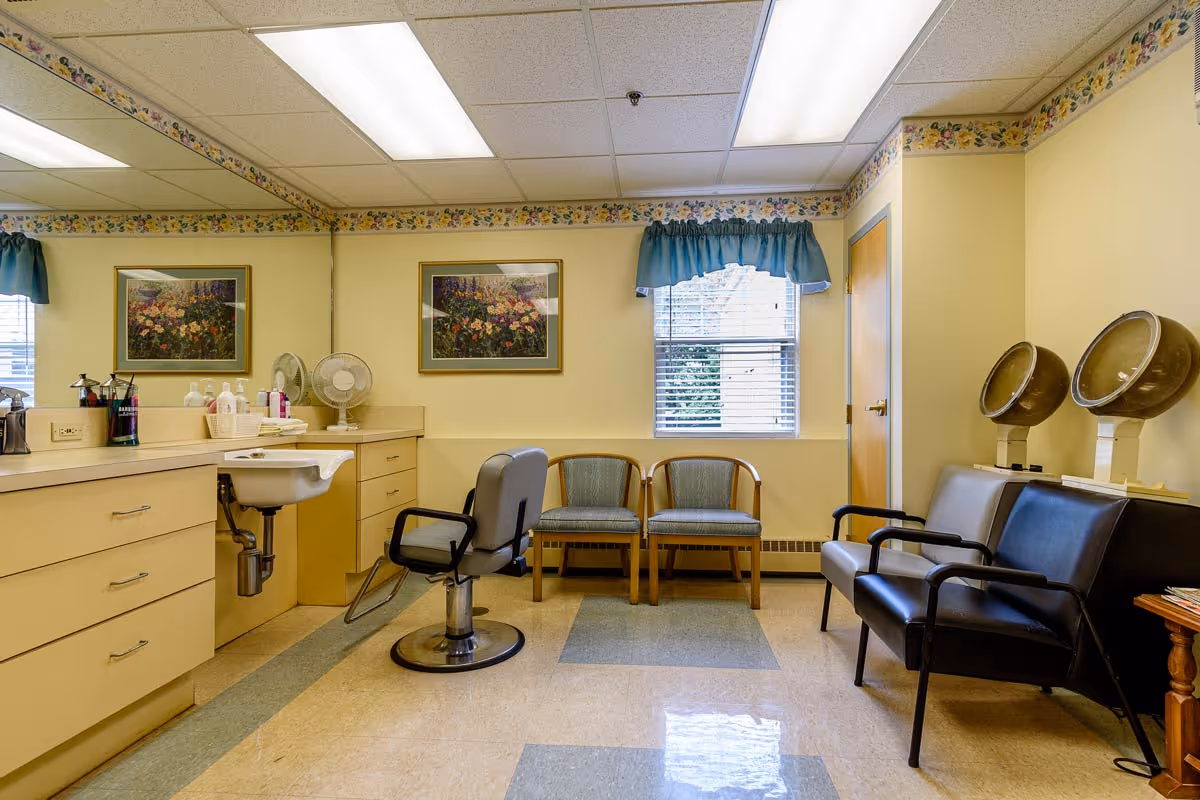 Interior salon room with a styling chair, sink and counters, waiting chairs and hooded hair dryers.