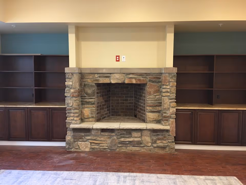 Stone fireplace centered between built-in dark wood cabinets and shelving in a communal living area.