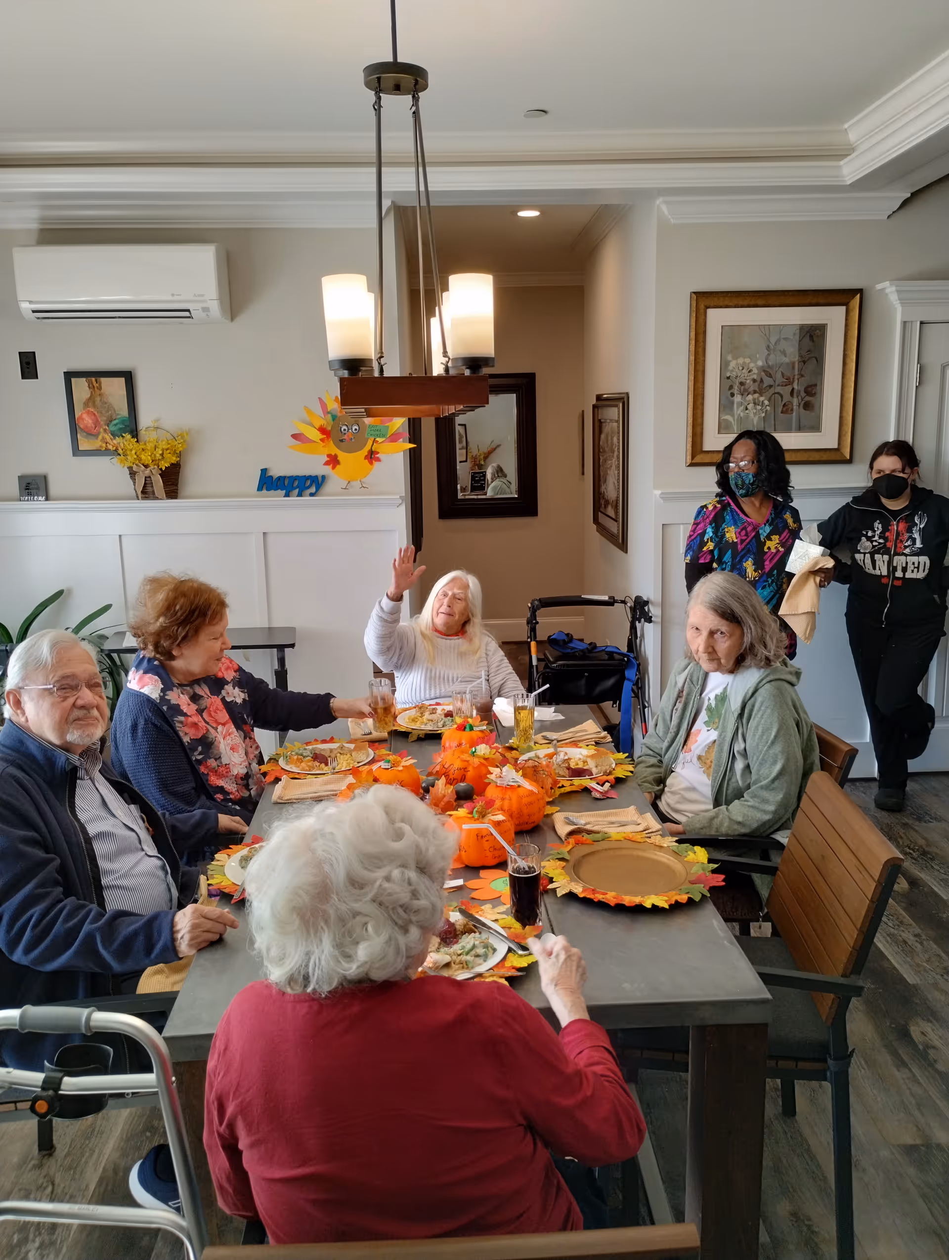 Several elderly residents and staff gathered around a festively decorated dining table inside a communal dining room.