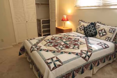 Bedroom with a patchwork quilt bedspread, nightstand lamp, and open closet.