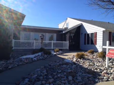 Front view of a single-story assisted living building with a rocky landscape and porch.