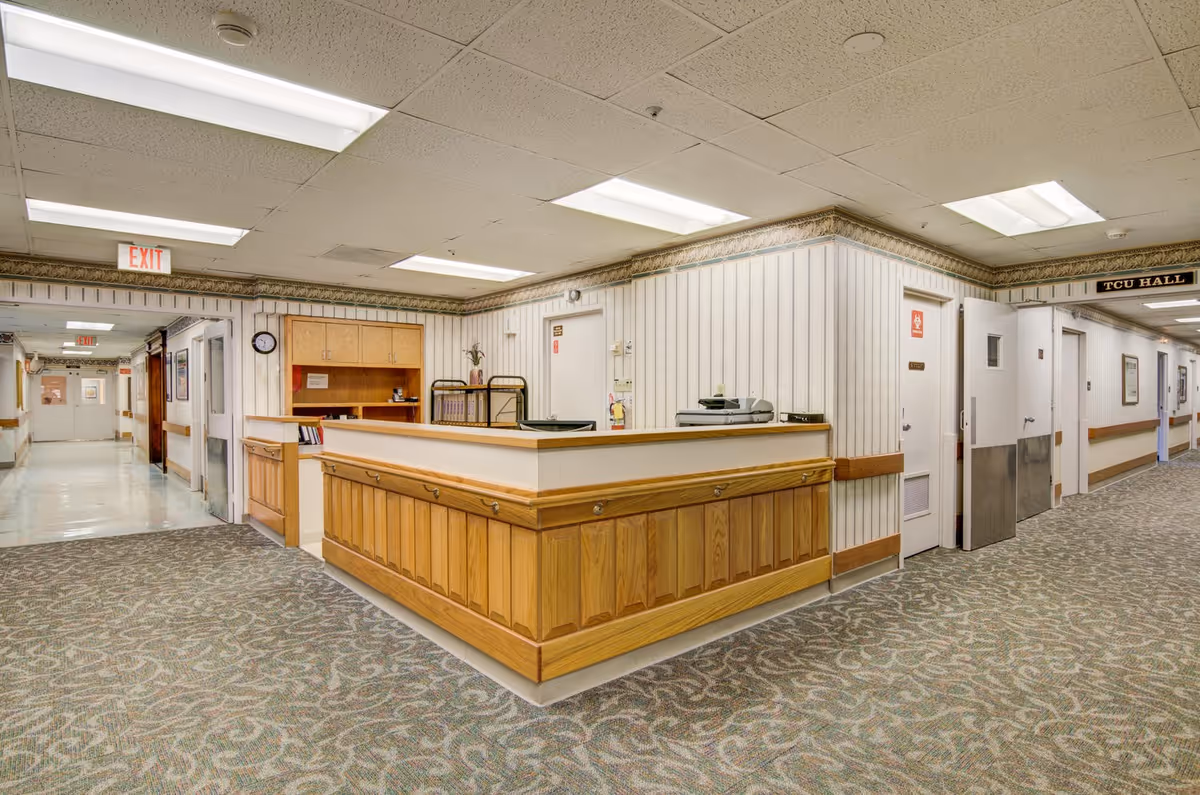 Reception desk and nursing station in a carpeted hallway of a senior living facility interior.