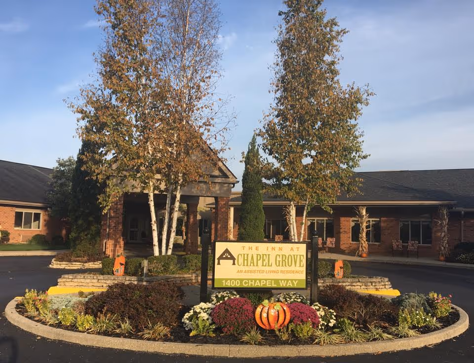 Front entrance of The Inn at Chapel Grove with a landscaped circular driveway, sign, and seasonal pumpkins.