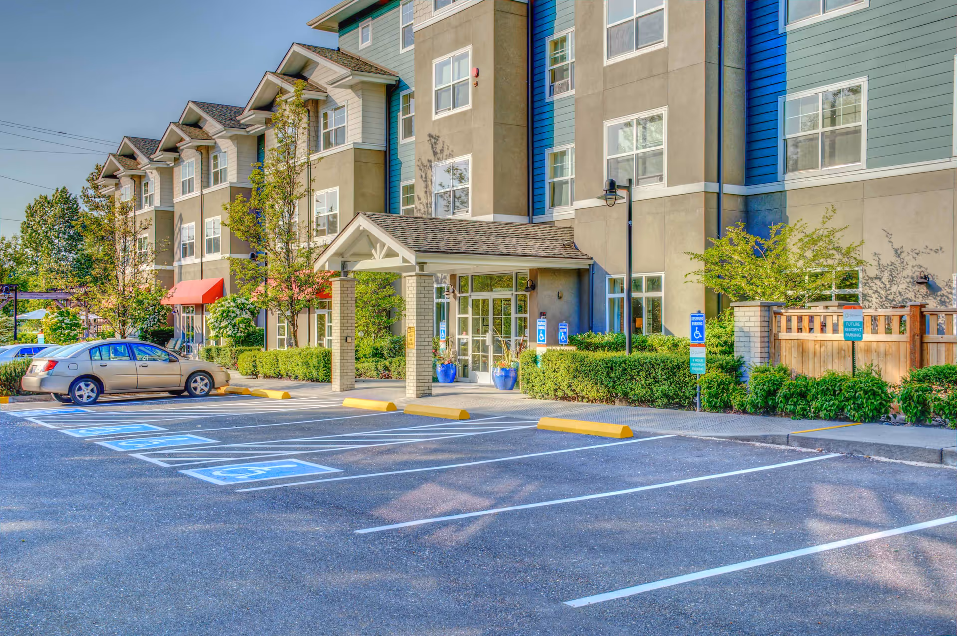 Front entrance of a multi-story senior living building with a covered entry, accessible parking spaces, and landscaping.