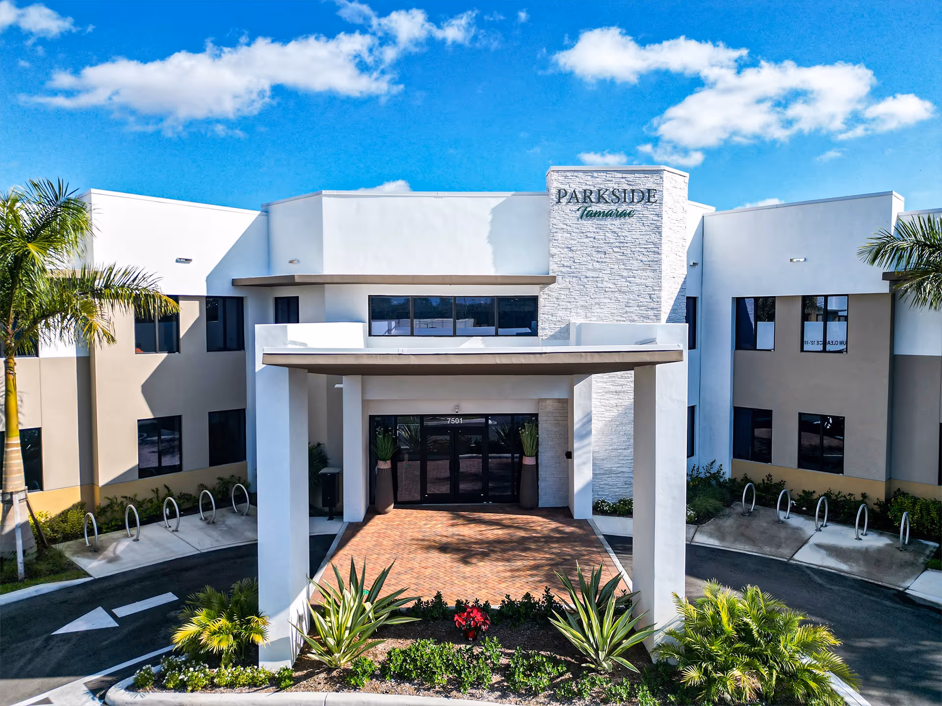 Front entrance of the Parkside Tamarac building with a porte-cochere, landscaping, and visible signage.