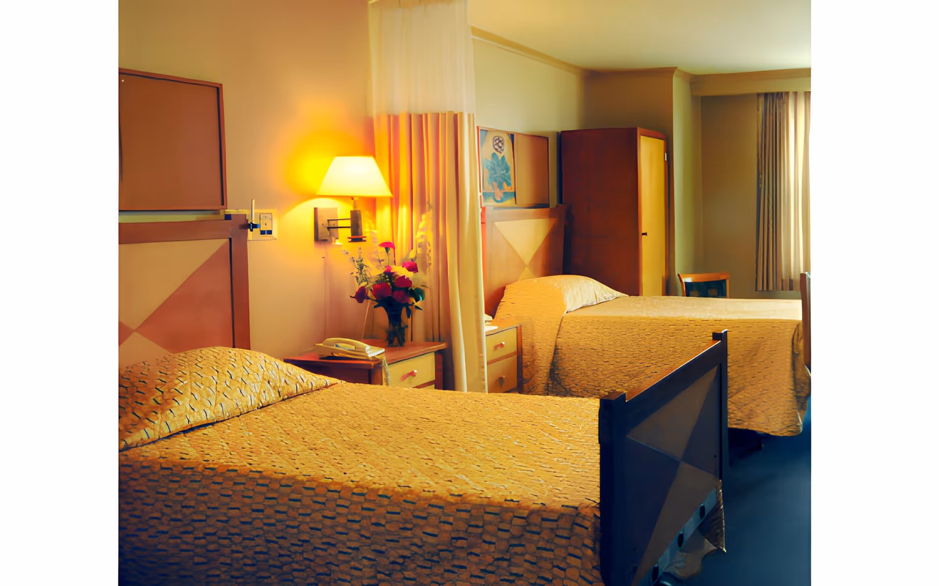 Two twin beds in a senior living facility room with a nightstand, lamp, wardrobe and a window with curtains.