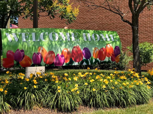Exterior view of a brick facility with a colorful Welcome Home banner and yellow flowers.